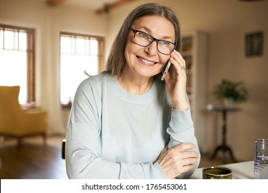 Attractive Mature European Woman Having Phone Conversation, Sharing News With Her Daughter, Smiling. Senior Female Speaking On Mobile At Home. Technology, Communication And Aged People Concept