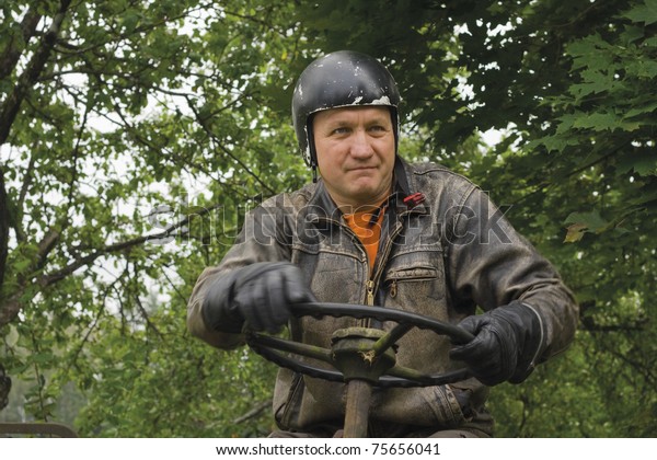 Attractive mature man with a black helmet on head,\
dressed in black leather gloves and an old leather jacket, steered\
old cars
