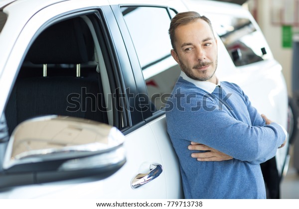 Attractive mature man posing at the car dealership
leaning on his new auto smiling joyfully to the camera copyspace
positivity driving license purchase sales offer insurance rental
service lease