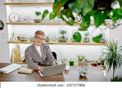 Attractive Mature Woman Doing Business Work Using Laptop, Modern Technologies. Senior Woman Wearing Glasses Sit In Light Office