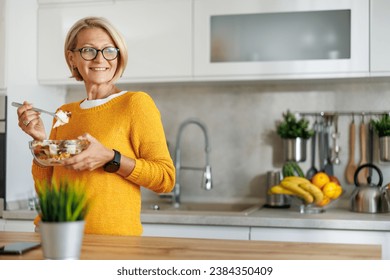 Attractive mature woman eating salads in her kitchen.Mature woman eating salads at home. - Powered by Shutterstock