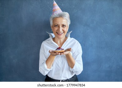 Attractive Mature Woman With Gray Haired Eating Birthday Cake. Elegant Middle Aged In White Shirt Celebrating Anniversary Posing Isolated With Freshly Baked Pie, Having Joyful Facial Expression