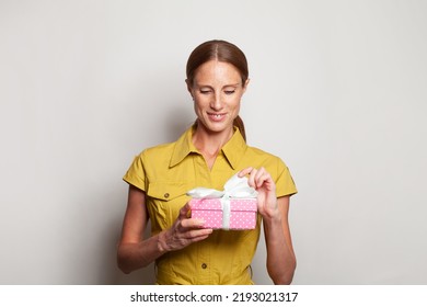 Attractive Mature Woman Opening Pink Gift Against White Studio Wall Background