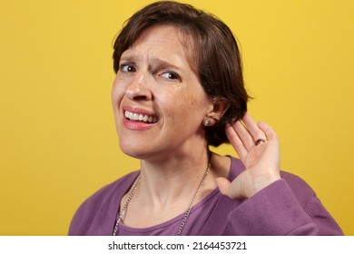 Attractive Mature Woman In Purple Blouse On A Yellow Background Can't Hear. Difficulty Hearing Concept Image.