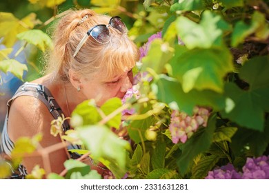 Attractive mature woman smelling beautiful pink hydrangea flowers outdoor - Powered by Shutterstock