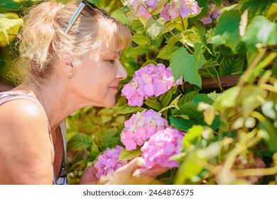 Attractive mature woman smelling beautiful pink hydrangea flowers outdoor - Powered by Shutterstock