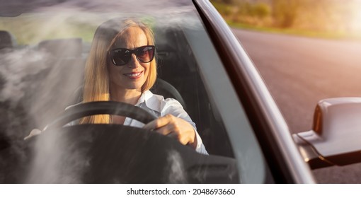 Attractive mature woman in sunglasses and formal wear looking at side mirror while driving car. View through windshield. Sunny weather outdoors. - Powered by Shutterstock