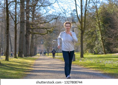 Attractive mature woman taking her daily jog through a wooded park approaching the camera along a tree lined avenue in a health and fitness concept - Powered by Shutterstock