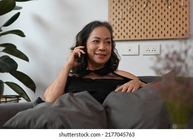 Attractive Mature Woman Talking On Mobile Phone, Resting On Couch At Home