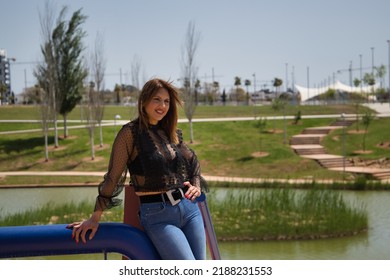 Attractive Mature Woman In Transparent Black Shirt And Jeans, Leaning On A Railing In Sensual And Provocative Attitude. Concept Maturity, Beauty, Fashion, Trend, Sensuality, Provocation.