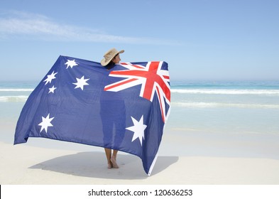 Attractive mature woman wearing akubra hat and with Australian flag around shoulder standing at tropical Australian beach, isolated with ocean and blue sky as background and copy space. - Powered by Shutterstock