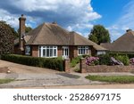 Attractive mid 20th century British red brick bungalow with pretty garden, and attached garage in a middle class suburban neighbourhood on a sunny summer day