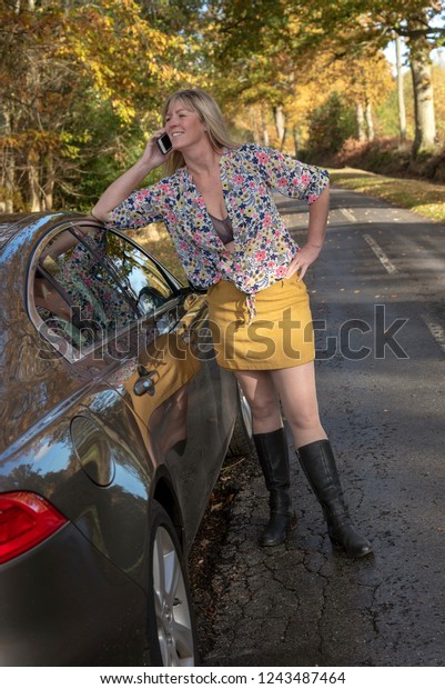 Attractive mid aged woman driver out of a\
car using a mobile telephone on a country\
road