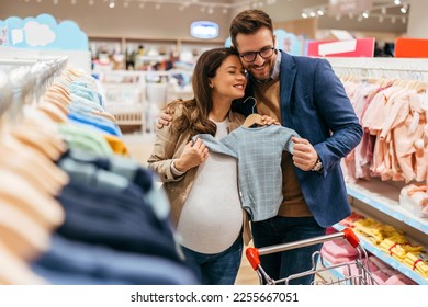 Attractive middle age couple enjoying in buying clothes and appliances for their new baby. Heterosexual couple in baby shop or store. Expecting baby concept. - Powered by Shutterstock