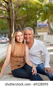 Attractive Middle Age Couple Posing In A Downtown Scene With Street And Trees In The Background.