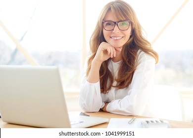 An attractive middle aged businesswoman sitting in front of laptop and managing her small business from home. 
