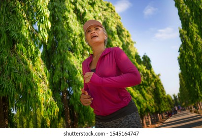 Attractive Middle Aged Lady Running Happy At City Park . Beautiful And Sporty Woman On Her 40s Exercising Doing Jogging Workout On A Sunny Morning Enjoying Healthy Lifestyle And Fitness