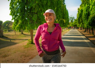 Attractive Middle Aged Lady Running Happy At City Park . Beautiful And Sporty Woman On Her 40s Exercising Doing Jogging Workout On A Sunny Morning Enjoying Healthy Lifestyle And Fitness