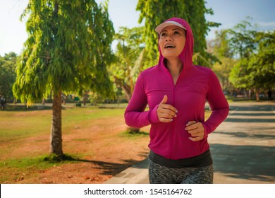 Attractive Middle Aged Lady Running Happy At City Park . Beautiful And Sporty Woman On Her 40s Exercising Doing Jogging Workout On A Sunny Morning Enjoying Healthy Lifestyle And Fitness