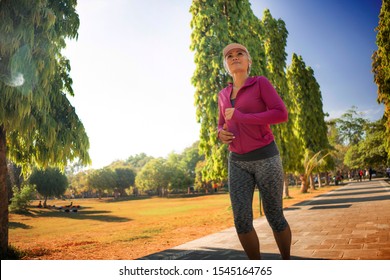 Attractive Middle Aged Lady Running Happy At City Park . Beautiful And Sporty Woman On Her 40s Exercising Doing Jogging Workout On A Sunny Morning Enjoying Healthy Lifestyle And Fitness