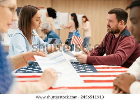 Attractive middle aged man, US citizen talking to polling station worker, sitting at registration table, writing ballot. Concept of USA presidential election, democracy, voting