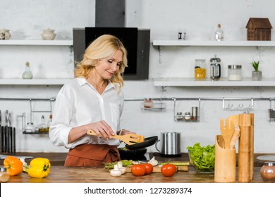 Attractive Middle Aged Woman Cooking Vegetables On Frying Pan In Kitchen