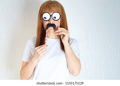 Attractive Middle Aged Woman Having Fun With A Fake Moustache And Glasses. A Woman In The Period Of Menopause.Blond / Red Hair Mature Senior Female Against The White Wall Background.