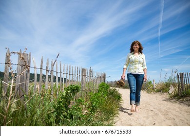 Attractive Middle Aged Woman Walking Barefoot Towards The Beach