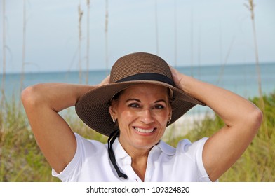 Attractive Middle Aged Woman Wearing A Sun Hat Standing On The Beach