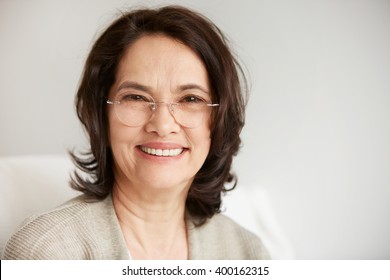 Attractive middle-aged brunette woman with a beautiful smile sitting against apartments background looking directly at the camera. Close up portrait of a senior middle aged lady relaxing at home.