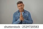 Attractive middle-aged man in a denim jacket posing with hands together against an isolated white background