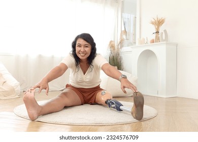 Attractive middle-aged woman with prosthetic leg doing exercise at home, happy disabled Asian female doing stretching on floor, cheerful sporty woman with disability doing warm-up before workout. - Powered by Shutterstock