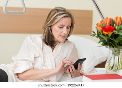 Attractive middle-aged woman sending a text message in hospital sitting up in her bed typing in information on her mobile phone - Powered by Shutterstock