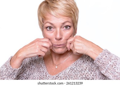 Attractive Middle-aged Woman With Short Blond Hair Trying To Reverse The Signs Of Aging By Pulling On Her Cheeks With Her Hands To Give Herself A Temporary Face Lift