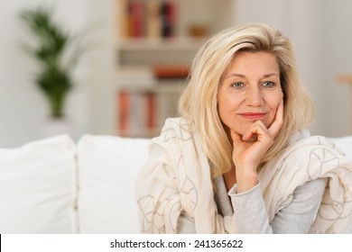 Attractive middle-aged woman sitting on a sofa at home daydreaming resting her chin on her hand staring to the side with a dreamy thoughtful expression