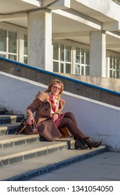 Attractive Middle-aged Woman Wearing Stylish Coat And Shoes Sitting With Bag On Stairs Of Building In Early Spring At Sunset. Street City Portrait, Fashion Urban Outfit. Dismissal From Office Concept