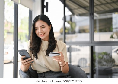 Attractive millennia Asian female holding her smartphone and credit card, using mobile banking app or online shopping app. - Powered by Shutterstock