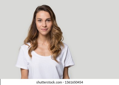 Attractive millennial female with curly hair wearing white t-shirt posing in studio over gray blank background smile looking at camera, copy space for your concept text advertisement head hot portrait