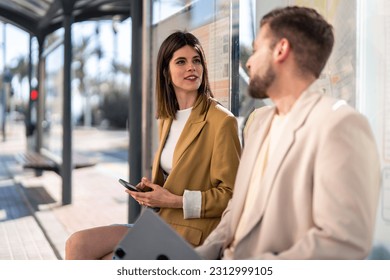 Attractive millennial woman having a conversation with man in beige suit while sitting at bus station and waiting for the bus to come. - Powered by Shutterstock