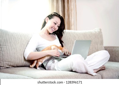 Attractive mixed asian woman with kitten on the couch using a laptop