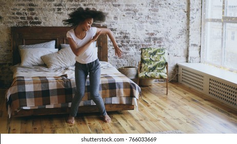 Attractive mixed race young joyful woman have fun dancing near bed at home