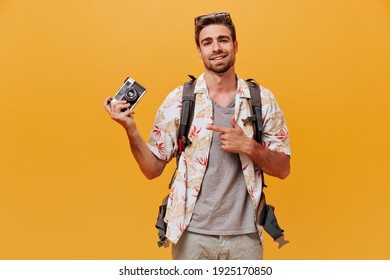 Attractive modern man with cool hairstyle in white printed shirt pointing to camera his finger and smiling on orange backdrop..