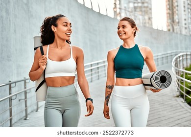 Attractive modern sports women walk holding mats for fitness training, yoga and joyfully chatting. Sincere friendship and sports lifestyle. - Powered by Shutterstock