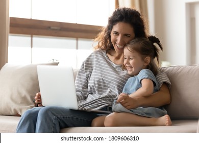 Attractive mother hug little daughter sitting on couch watching educational funny cartoons on pc laughing enjoy time together on weekend at home. Develop child and having fun using modern tech concept - Powered by Shutterstock