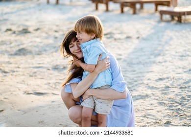 Attractive Mother And Hugging And Little Son Having Fun By The Lake Outdoors Enjoying Nature. Portrait Lovely Family Over Sunny Warm Light.