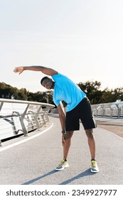 Attractive muscular african american man wearing blue t hirt warming up lening to the side before running, copy space. Handsome young man stretching, favorite hobby. Concept of motivation, contraction