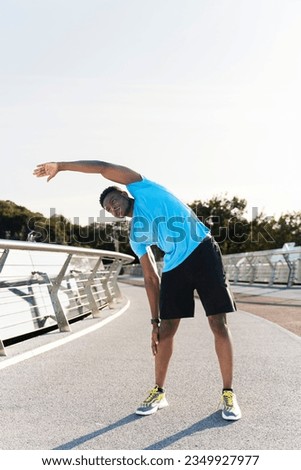 Attractive muscular african american man wearing blue t hirt warming up lening to the side before running, copy space. Handsome young man stretching, favorite hobby. Concept of motivation, contraction