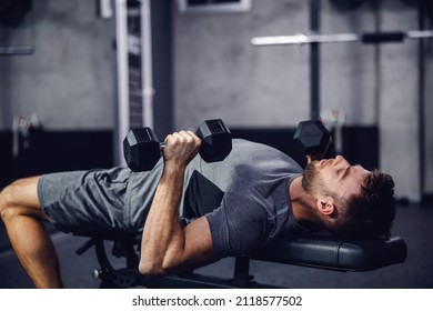 Ein attraktiver und muskulöser Mann bereitet sich darauf vor, Gewichte zu heben. Ein Sportler pumpt seine Armmuskeln und hebt die Hantel in einem modernen Fitnessraum auf. Nahaufnahme eines männlichen Menschen, der auf einer Sportbank liegt. Sport