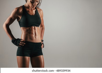 Attractive Muscular Woman With Gloved Hands On Hips Showing Off Her Strong Abs Over Gray Background