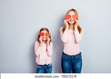 Attractive, nice, cute, sweet, charming daughter and mom, mum standing over gray background, holding four small paper hearts on eyes place, smiling, having fun